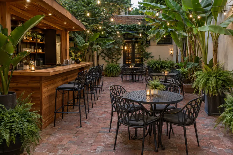 Concept image of a restaurant courtyard with brick pavers, a cedar outdoor bar, string lights and tropical plants.