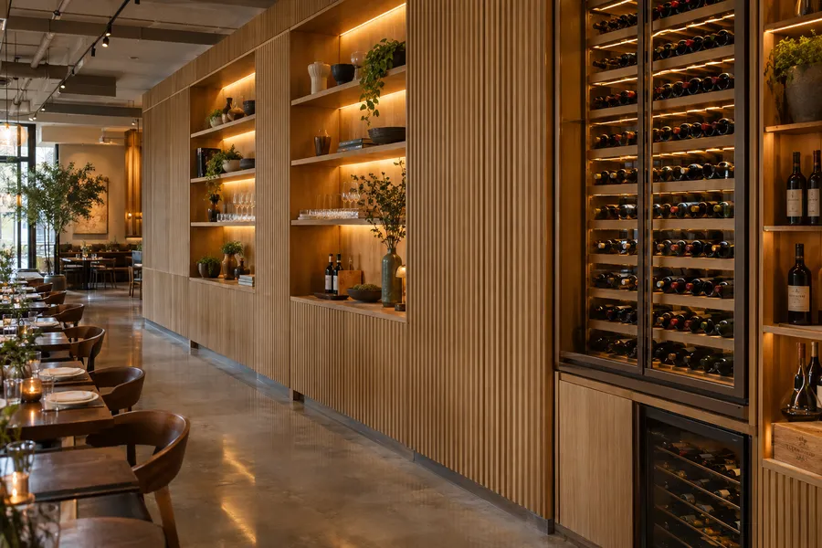 Concept image of fluted white oak wall paneling with lit display shelving and a built-in wine wall in a restaurant.