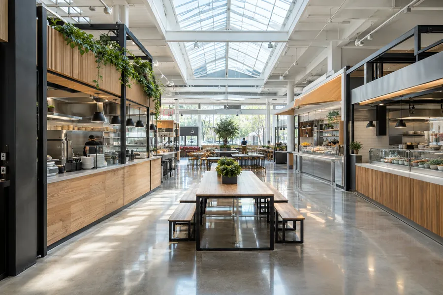 Concept image of a modern food hall with custom wood-and-steel vendor stalls, communal tables and skylights.