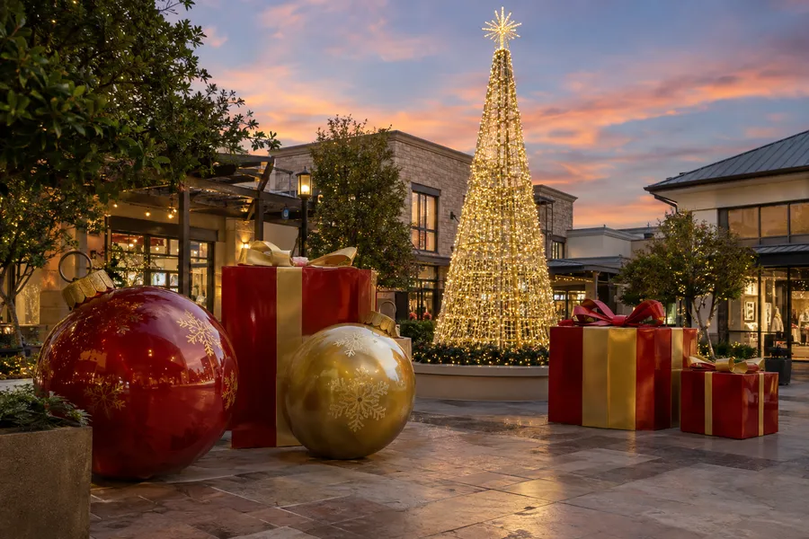 Concept image of oversized holiday props in a shopping plaza: giant ornaments, wrapped gift boxes and an illuminated tree sculpture.