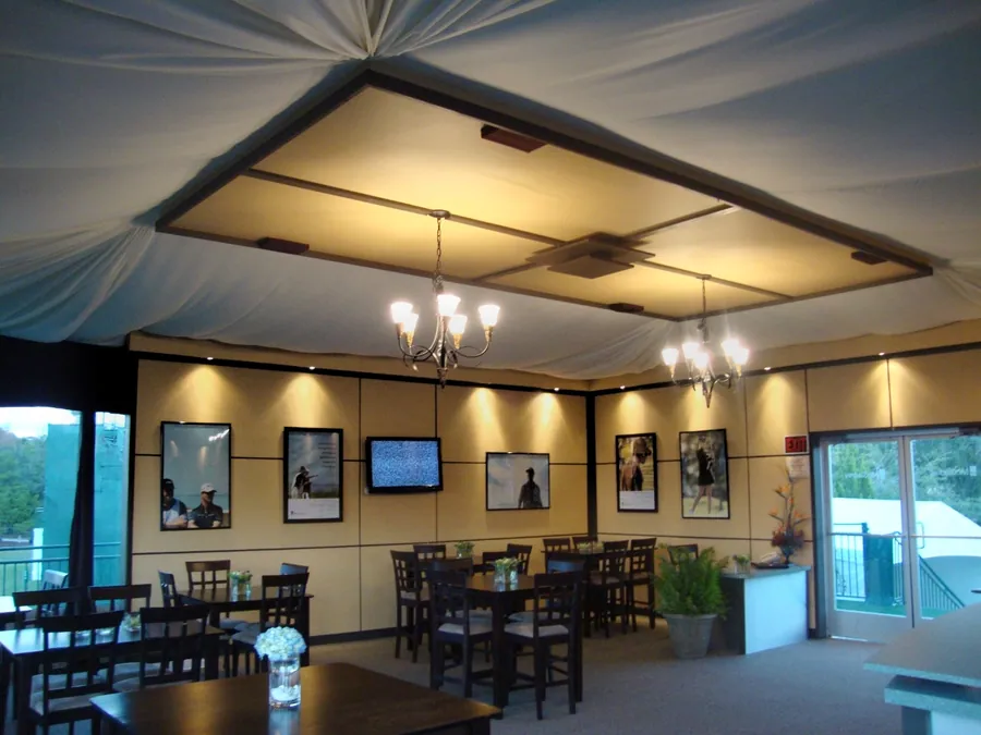 A tented room with a draped and framed ceiling, chandeliers, framed photographic prints on the walls, and dark timber tables and chairs.