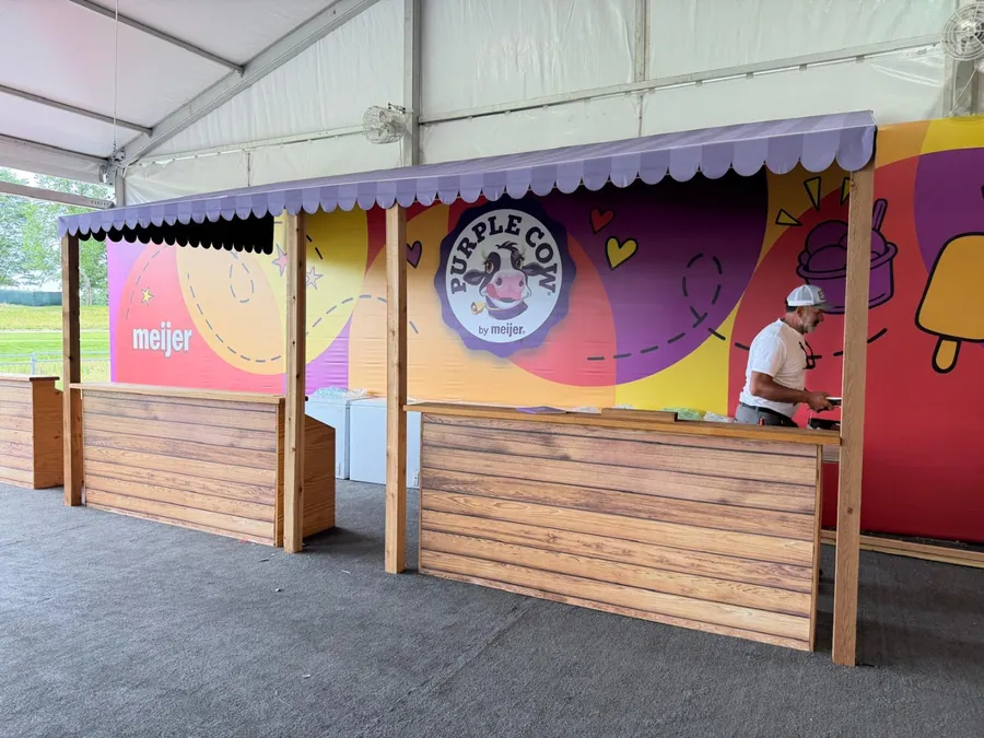 A brightly coloured activation counter with a scalloped canopy and bold printed graphics, staffed under a white tent.