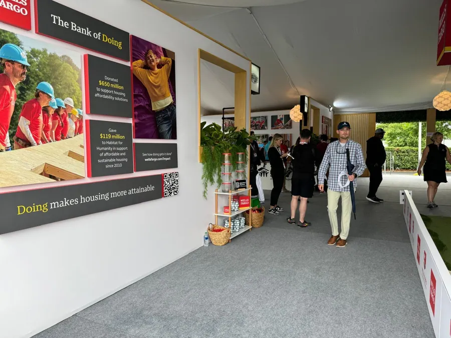 Guests walking through a tented arrival corridor lined with large printed brand panels and planted greenery.