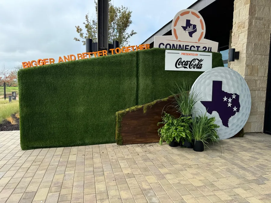 An outdoor Connect turf wall with a Texas medallion, Coca-Cola sign, wood panel and planters.