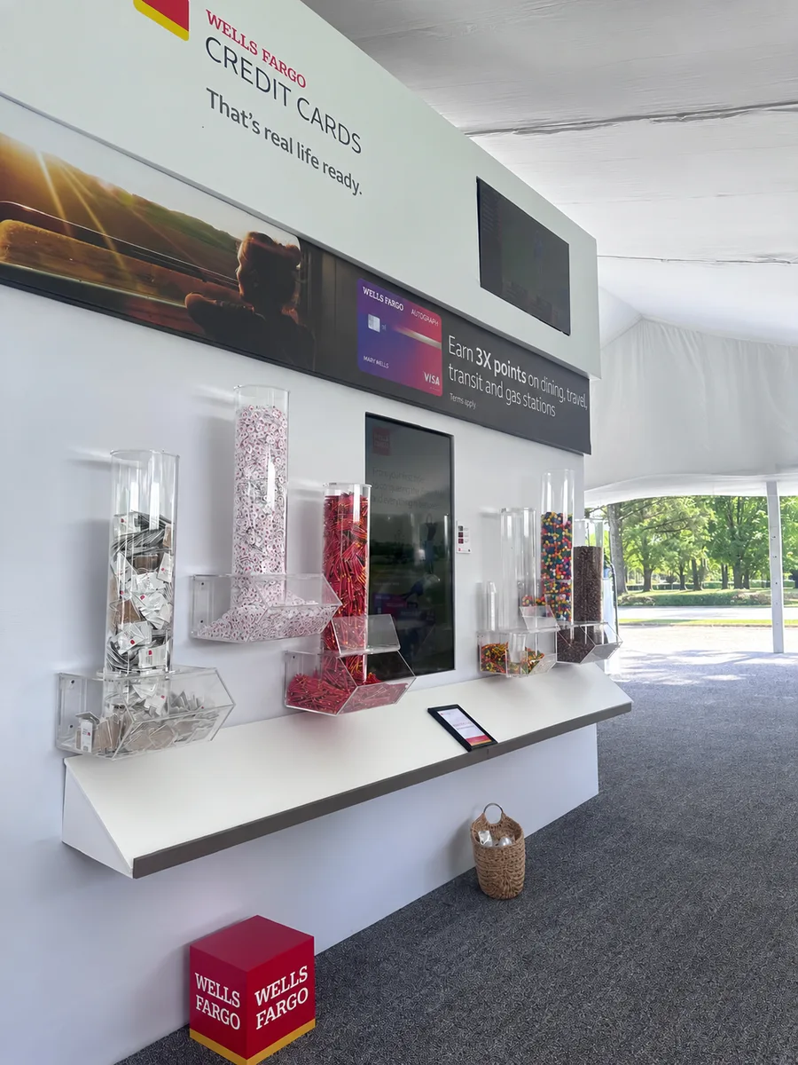 The completed Wells Fargo Credit Cards candy wall with acrylic dispensers, screens and branded header inside a tournament hospitality tent.