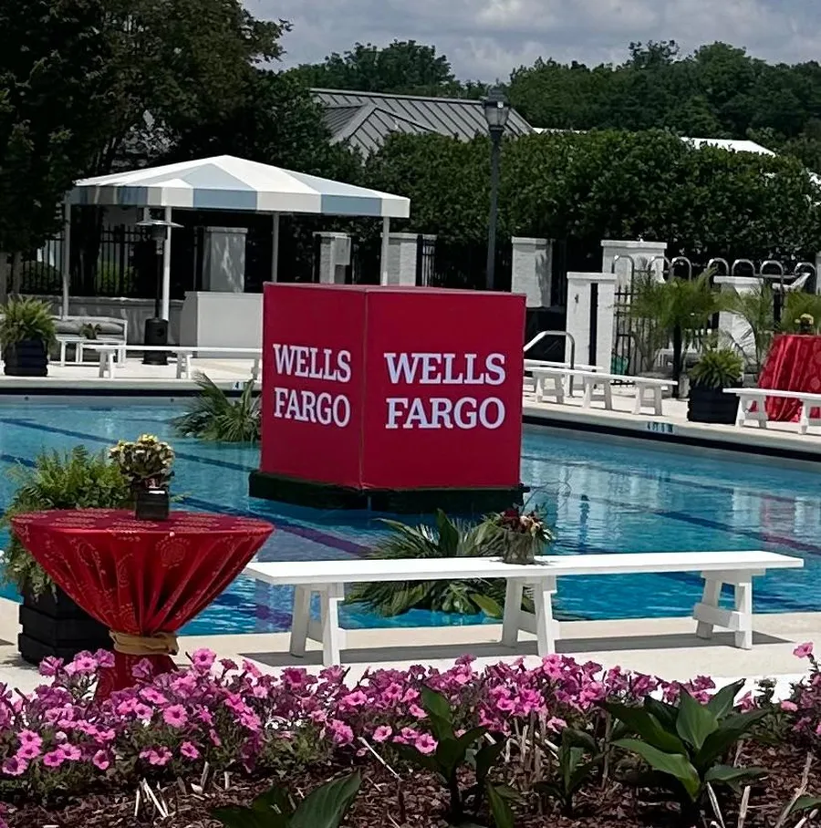 A Wells Fargo branded cube floating in a pool beside a hospitality lounge with flowers and white benches.