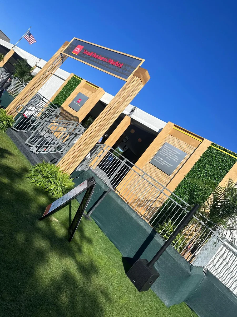A timber-framed hospitality structure with a branded sign bar and greenery walls on a golf course.